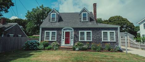 A two-story house with a red door, white trim, and a small front porch.
