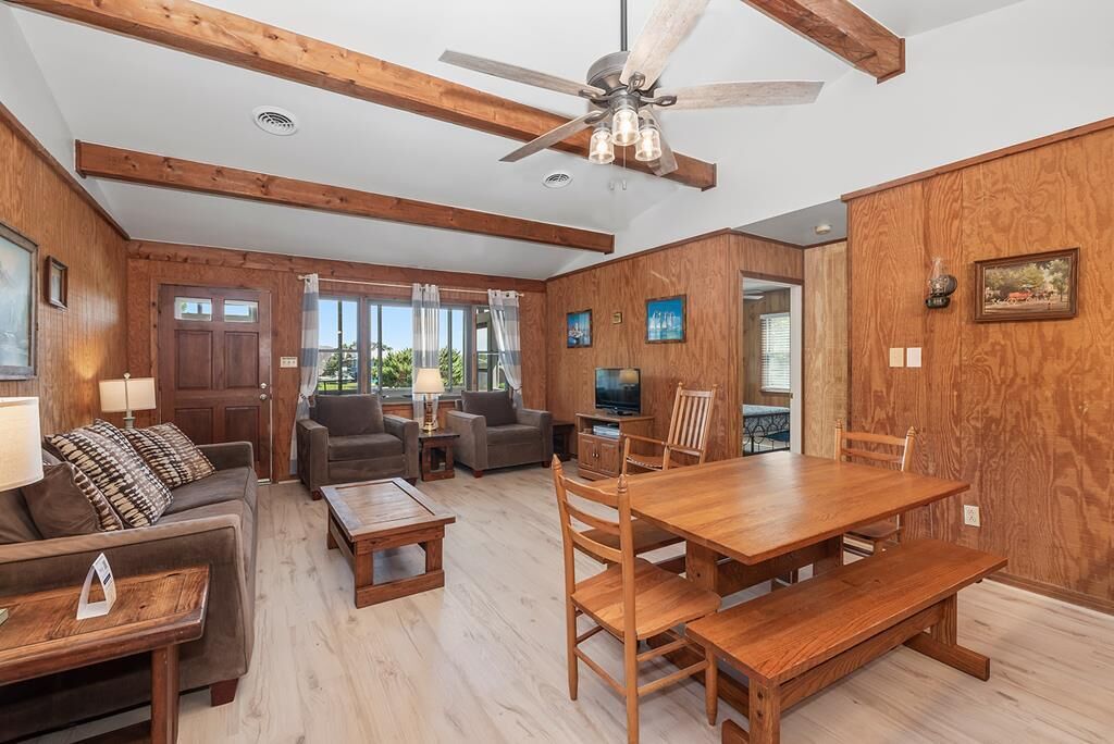 A spacious living room with wooden floors, a ceiling fan, and a dining area with a wooden table and chairs.