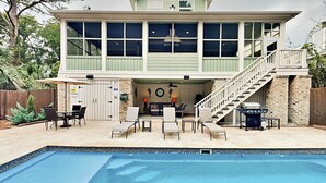 A two-story house with a pool, outdoor seating, and a staircase leading to the upper level.