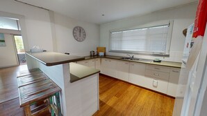 Una cocina con una mesa de madera, armarios blancos, un reloj y una ventana con persianas.