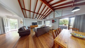 Un salón amplio con techo de madera, un sofá, una mesa de comedor y un televisor.