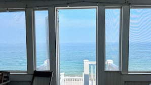 Una habitación con amplios ventanales que dan al océano, una terraza de madera y una silla.