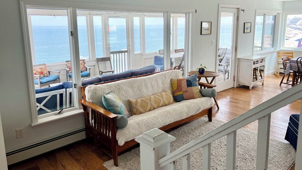 Una sala de estar acogedora con un ventanal grande con vistas al mar, un banco de madera y un comedor con mesa y sillas.