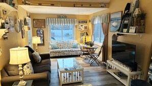 A living room with a sofa, coffee table, TV, and a dining area with a table and chairs. - Lake Erie Beach House In Quiet Communitty. (Huron)