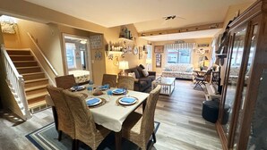 A dining area with a table set for four, surrounded by wicker chairs. A staircase is visible to the left, leading to another level. - Lake Erie Beach House In Quiet Communitty. (Huron)