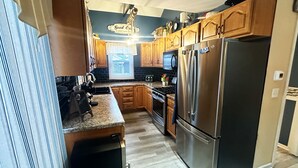 A modern kitchen with wooden cabinets, a stainless steel refrigerator, a built-in oven, and a window with blinds. - Lake Erie Beach House In Quiet Communitty. (Huron)