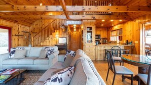 Een gezellig cabin interieur met een zithoek, eethoek, keuken en een trap naar een vide.