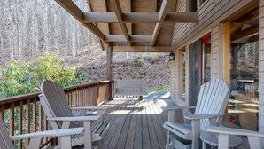 Een houten terras met Adirondack-stoelen en een bankje, met uitzicht op een bebost gebied.