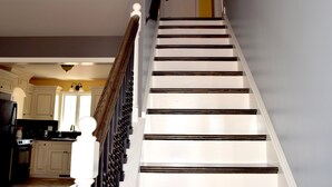 Un escalier avec des marches blanches et des balustrades sombres, menant à une porte dotée d’une poignée noire.