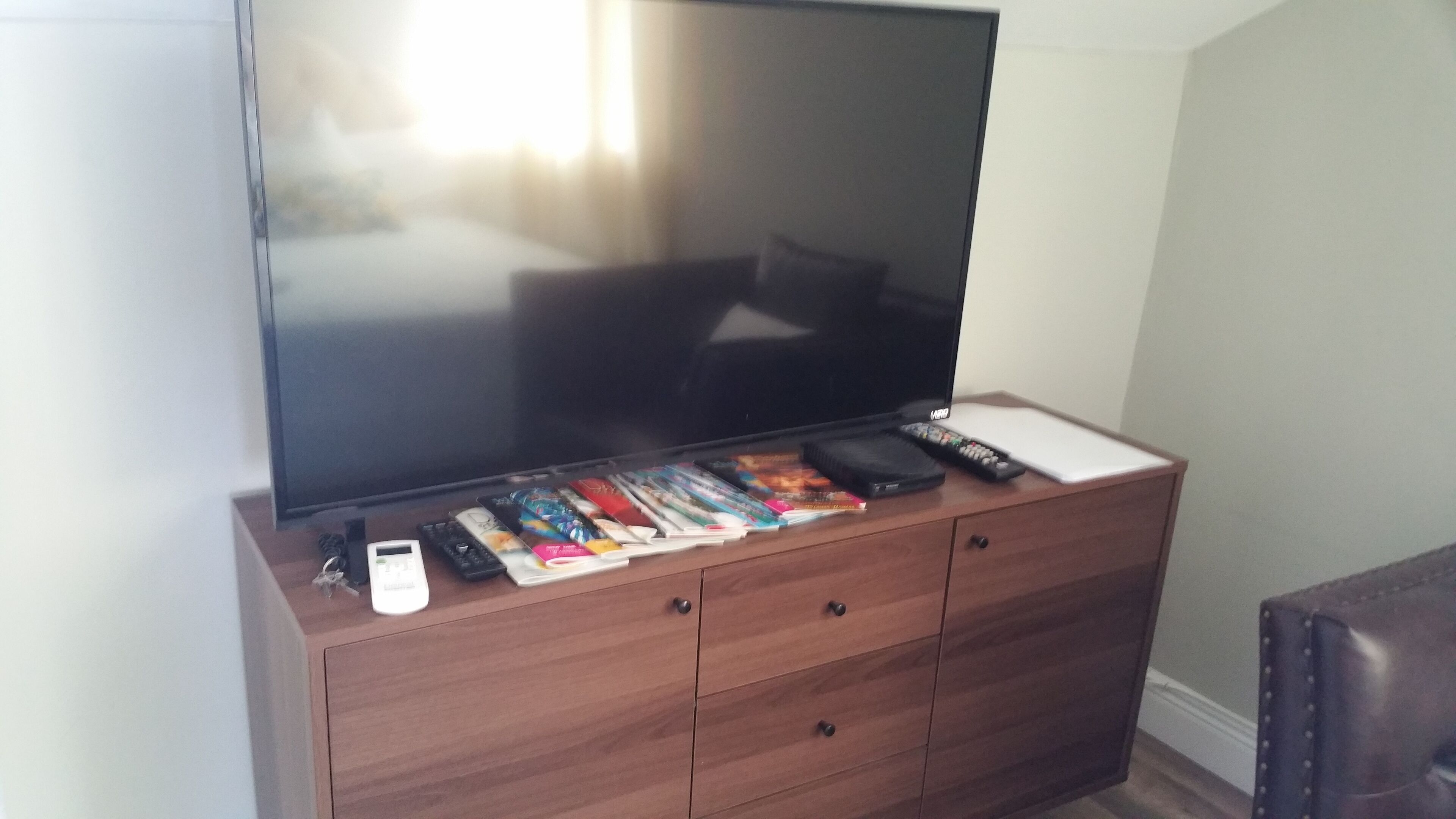 A wooden TV stand with a flat-screen TV, a remote control, a smartphone, and a wallet.