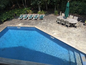 Piscina rectangular con solárium de baldosas, rodeada de sillones de descanso y una mesa con sillas.