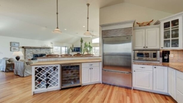 Una cocina amplia con piso de madera, armarios blancos, un refrigerador para vinos empotrado e iluminación colgante.