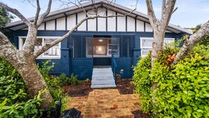 Une maison moderne à l’extérieur bleu foncé, dotée d’un porche et d’un chemin en briques menant à l’entrée.