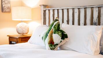 A bed with white bedding and a decorative pillow with a tropical leaf pattern.