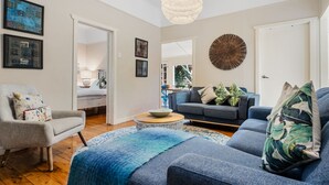 Un salon moderne avec un canapé gris, un canapé bleu, une table basse ronde et un tapis à motifs. Les murs sont ornés d’œuvres d’art encadrées et d’une grande décoration murale circulaire.