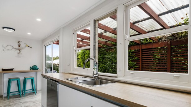 Une cuisine moderne avec des meubles blancs, un plan de travail en bois et une grande fenêtre donnant sur un paysage verdoyant.