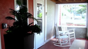 A porch with a rocking chair, a potted plant, and a view of the street. - SEAS THE DAY: Charming Folly Beach Apartment awaits your arrival! (Folly Beach)
