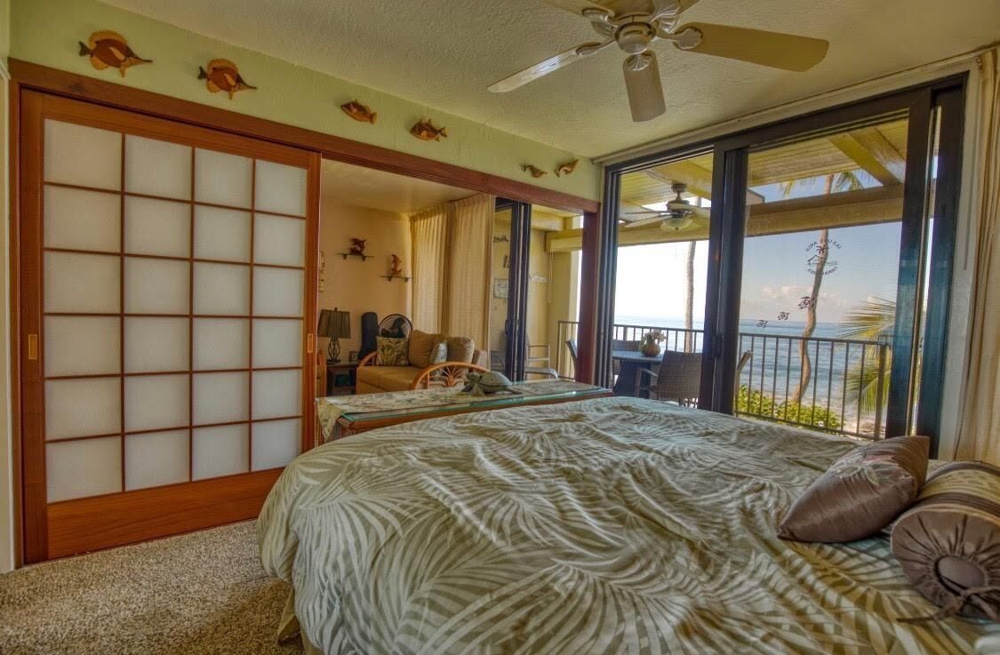 A hotel room with a bed, a chair, a table, and a view of the ocean.