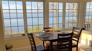 A dining area with a table and chairs, large windows with a view of a lake, and a ceiling fan. - Ocean Front cottage in Belfast (Belfast)