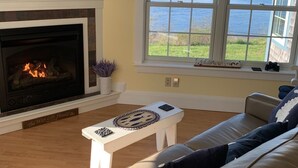 A living room with a fireplace, a television, a sofa, and a large window overlooking the sea. - Ocean Front cottage in Belfast (Belfast)