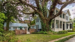 Une maison à deux étages avec un porche, entourée d’une pelouse bien entretenue et de grands arbres.