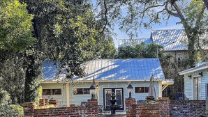 Un bâtiment de style rustique, avec une entrée surmontée d’un mur en briques, un patio couvert agrémenté de mobilier d’extérieur et un toit équipé de panneaux solaires.