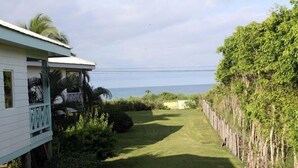 A white building with a balcony, a well-maintained lawn, and a view of the ocean. - Private Oceanview Bungalow #9 (Playa Hermosa)