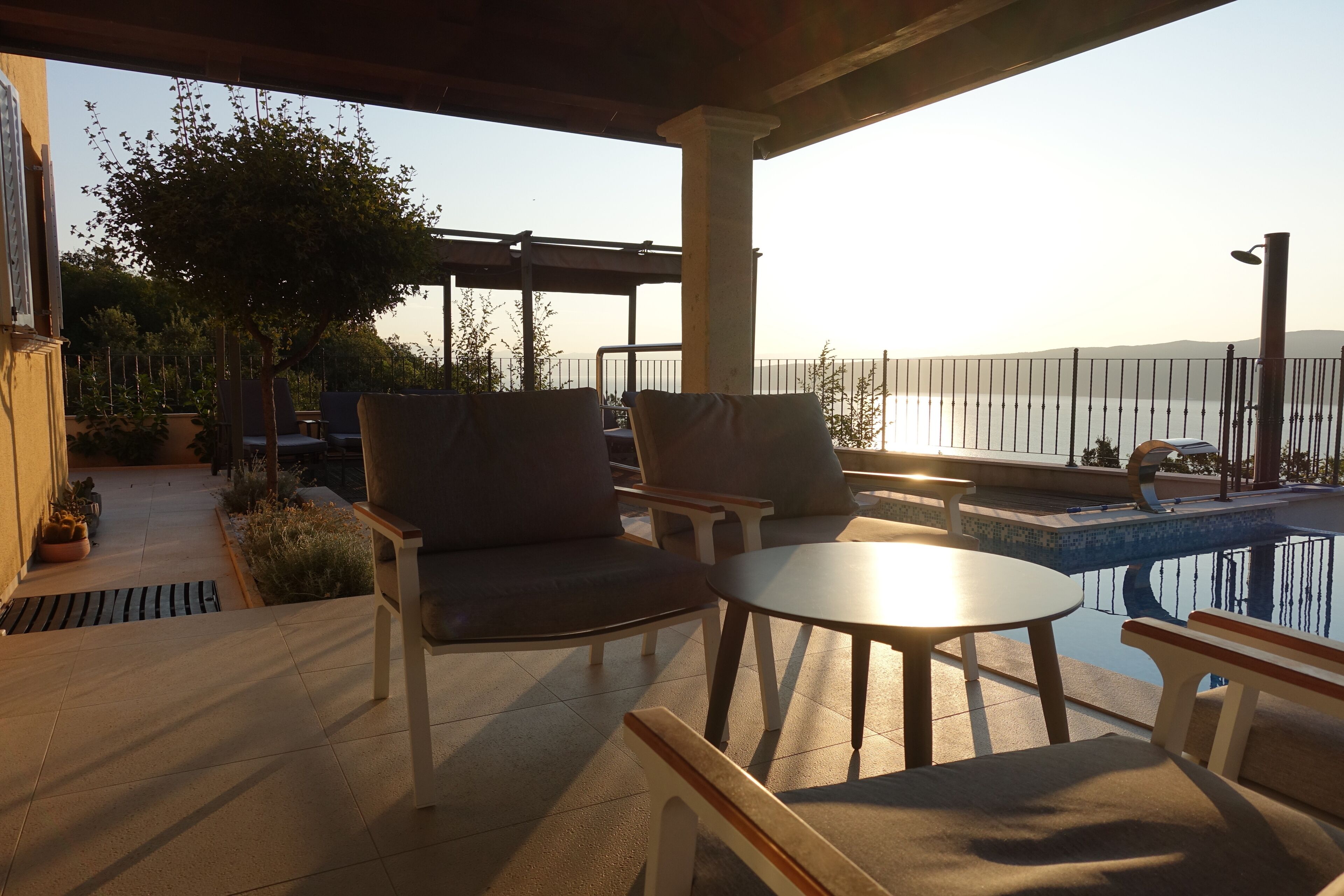 En patio med pool, udendørs møbler og havudsigt.