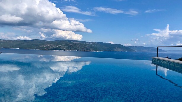Een zwembad zonder rand met helderblauw water dat de lucht en bergen weerspiegelt.