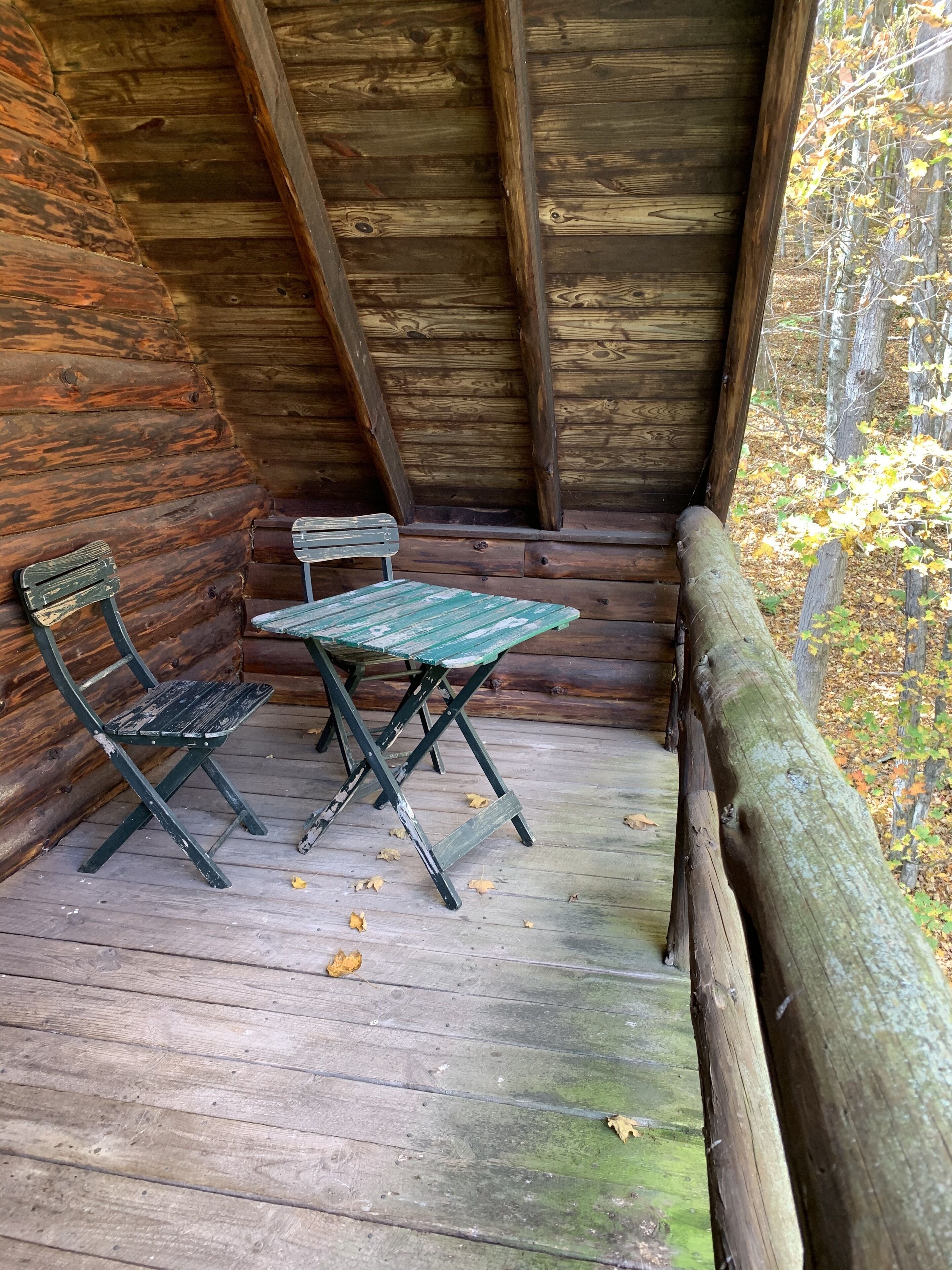 A rustic wooden cabin with a wooden deck, a bench, and a table.