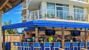A bar area with a poolside view, outdoor seating, and a bar counter.