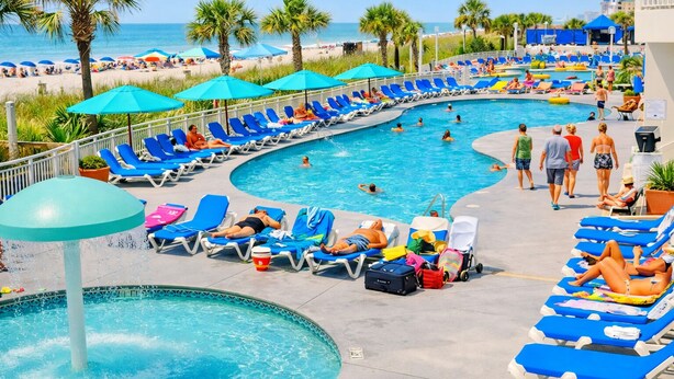 A pool area with lounge chairs, a water feature, and a view of the beach.