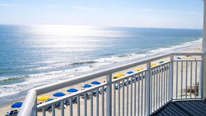 A balcony with a view of the ocean, beach chairs, and umbrellas.