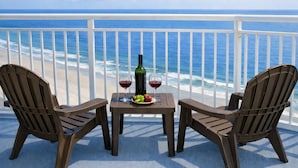 A balcony with two Adirondack chairs, a small table, a bottle of wine, and a glass of wine.