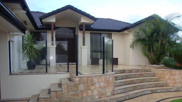 A modern house with a stone staircase leading to a glass door entrance, surrounded by a well-maintained lawn and palm trees. - Kooroora House -Spa Bath-Pool- Billard Table (Robina)