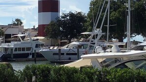 Um farol com bandeiras americanas, barcos atracados por perto e um céu claro.