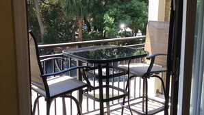 A balcony with a table and chairs, a view of trees, and a building in the background. - Summer is booking fast! Please book soon. New paint and upgrades!!! (Hilton Head Island)