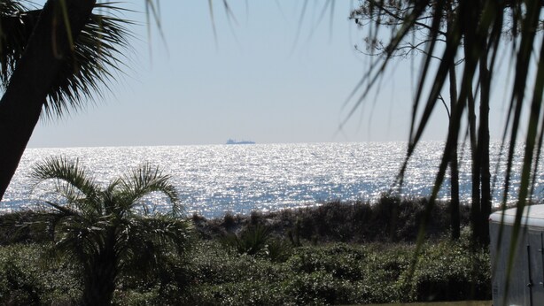 A view of a body of water with a ship in the distance, palm trees, and a building in the foreground. - Summer is booking fast! Please book soon. New paint and upgrades!!! (Hilton Head Island)