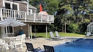 A backyard with a swimming pool, lounge chairs, a covered patio, and a deck with a railing. - Katama House w/Guest House w/AC South Beach heated pool. 
Summer weeks avail. 
 (Edgartown)