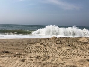 A beach with waves crashing onto the shore, sandy terrain, and footprints in the sand.