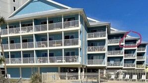 Un hotel de varios pisos con balcones, vista a la playa y un primer plano de arena.