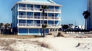 Un hotel de varios pisos con balcones, situado en una playa de arena con palmeras.