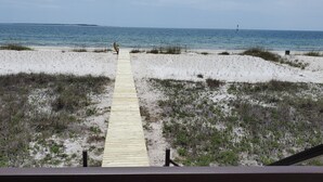 Ein hölzerner Steg führt zu einem Strand mit Dünen und dem Meer im Hintergrund.