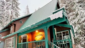 Ein mit Schnee bedecktes Haus mit Veranda und einem innen beleuchteten Bereich.