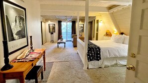 Ein Schlafzimmer mit einem Bett, einem Schreibtisch und einem Stuhl. Es gibt ein Fenster mit Vorhängen und ein Bild an der Wand.