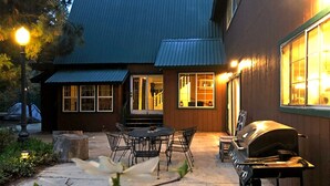 Eine Terrasse mit Grill und Essbereich, ein überdachter Sitzplatz im Freien sowie ein Gebäude mit großen Fenstern und einem Metalldach.