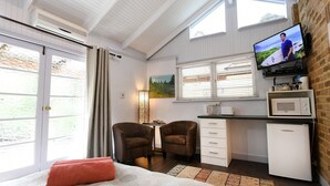 Een gezellige kamer met een bed, twee stoelen, een bureau met een computer, een televisie en een magnetron.