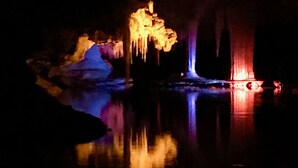 Een grot verlicht door kleurrijke lichten, weerspiegeld in het water.