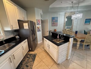 A kitchen with white cabinets, a stainless steel refrigerator, a black countertop, and a sink.