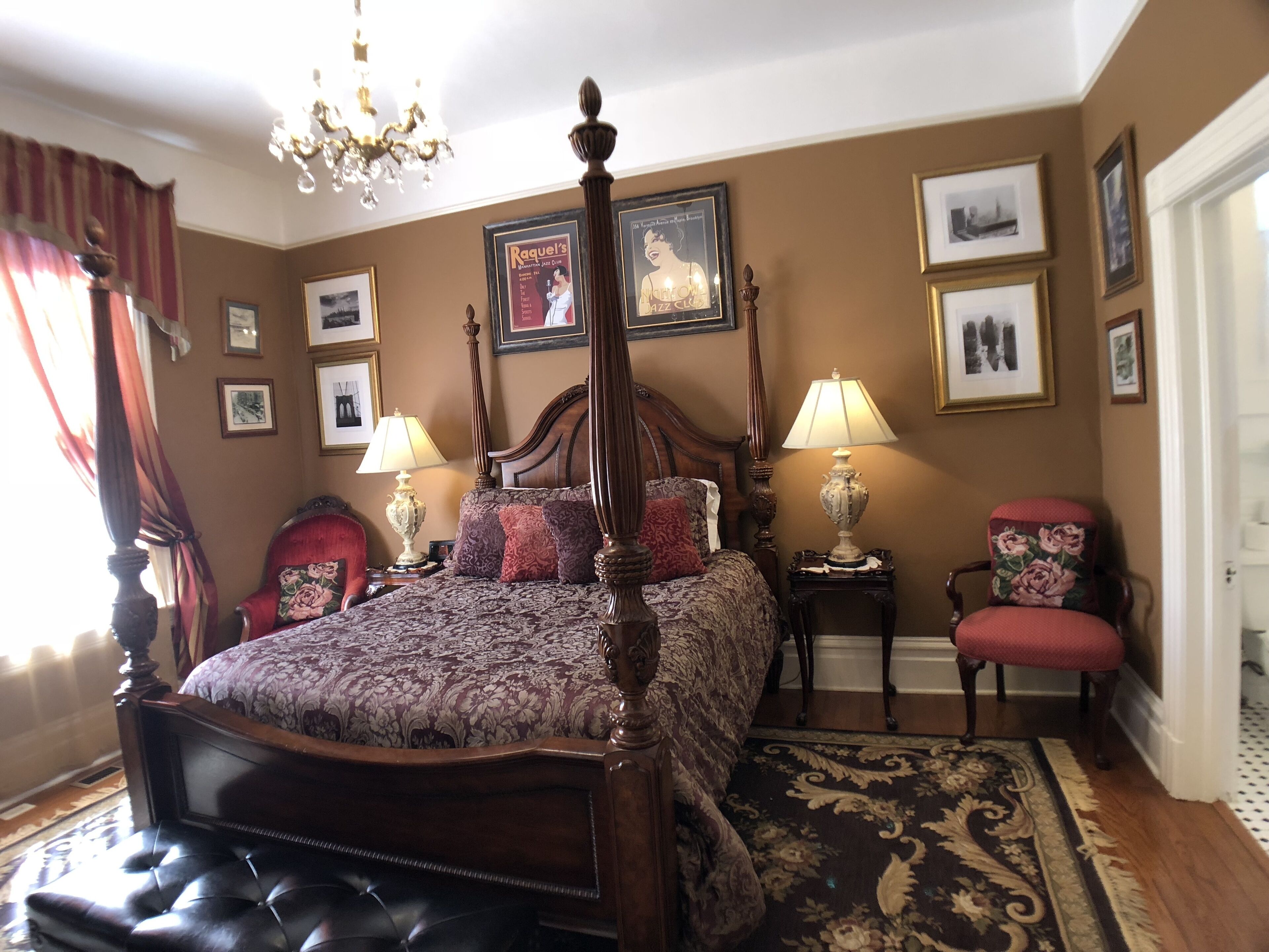 A bedroom with a four-poster bed, two bedside tables with lamps, a red armchair, and a patterned rug.